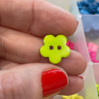 Hand holding a yellow flower-shaped button with a red nail polish, with more buttons in the background.