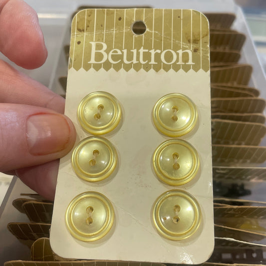 Packaging of gold buttons with 'Beutron' branding held by a hand.