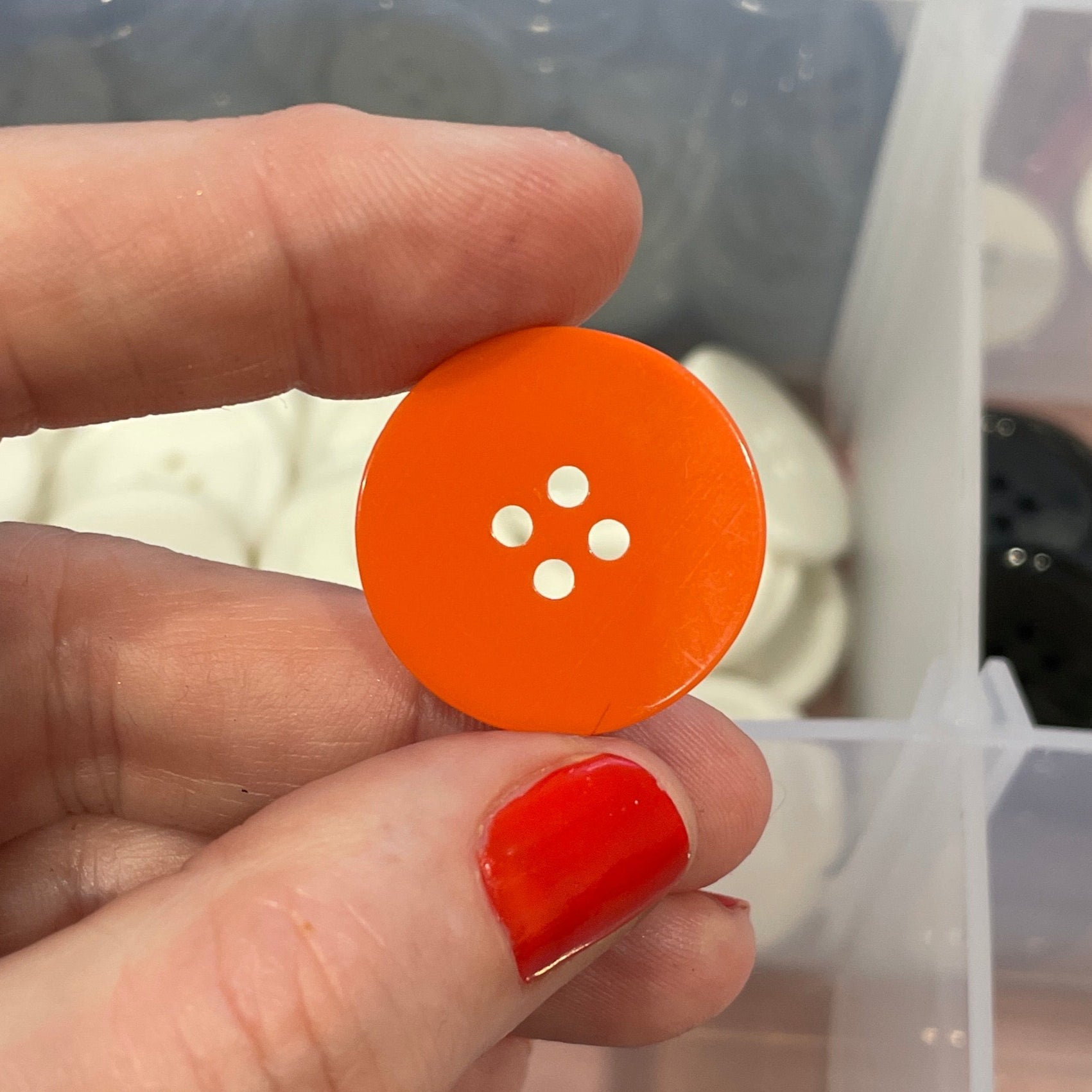 Hand holding an orange button with a clear container of buttons in the background