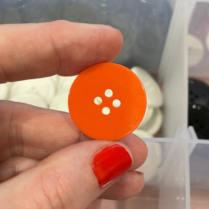 Hand holding an orange button with a clear container of buttons in the background