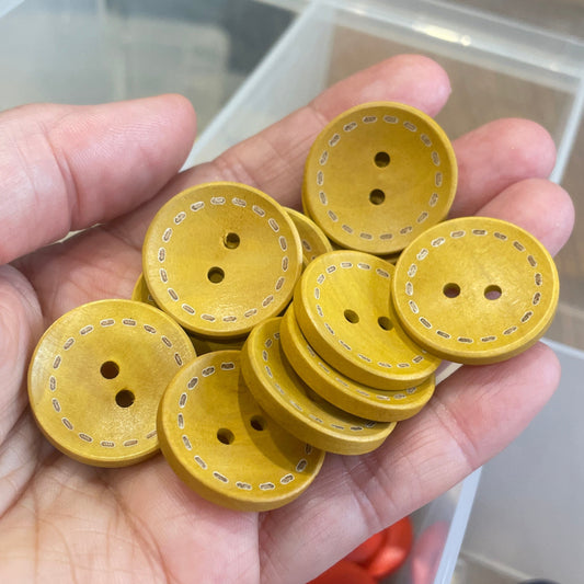 Hand holding yellow buttons with a container of colorful buttons in the background