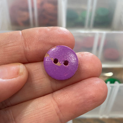 Hand holding a purple button with a clear container of buttons in the background