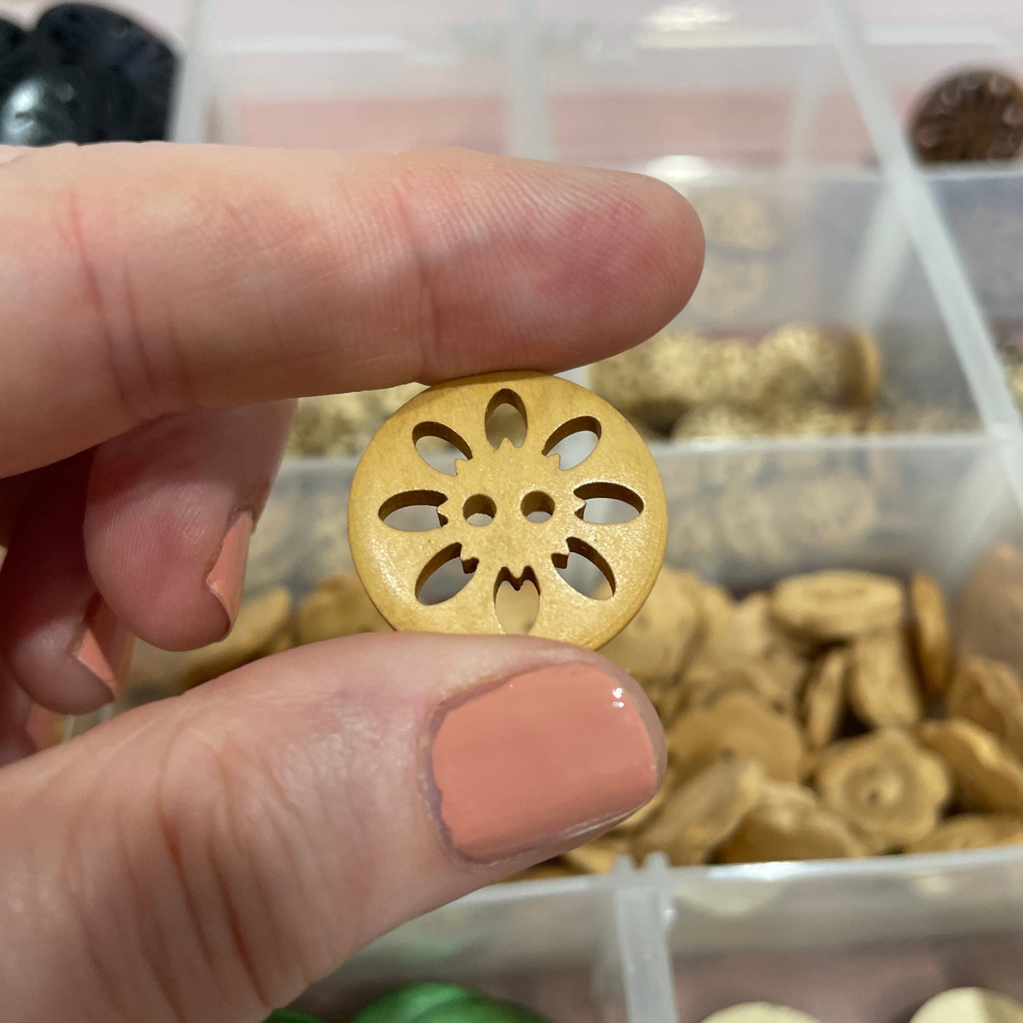 Gold decorative button held between two fingers with a container of buttons in the background