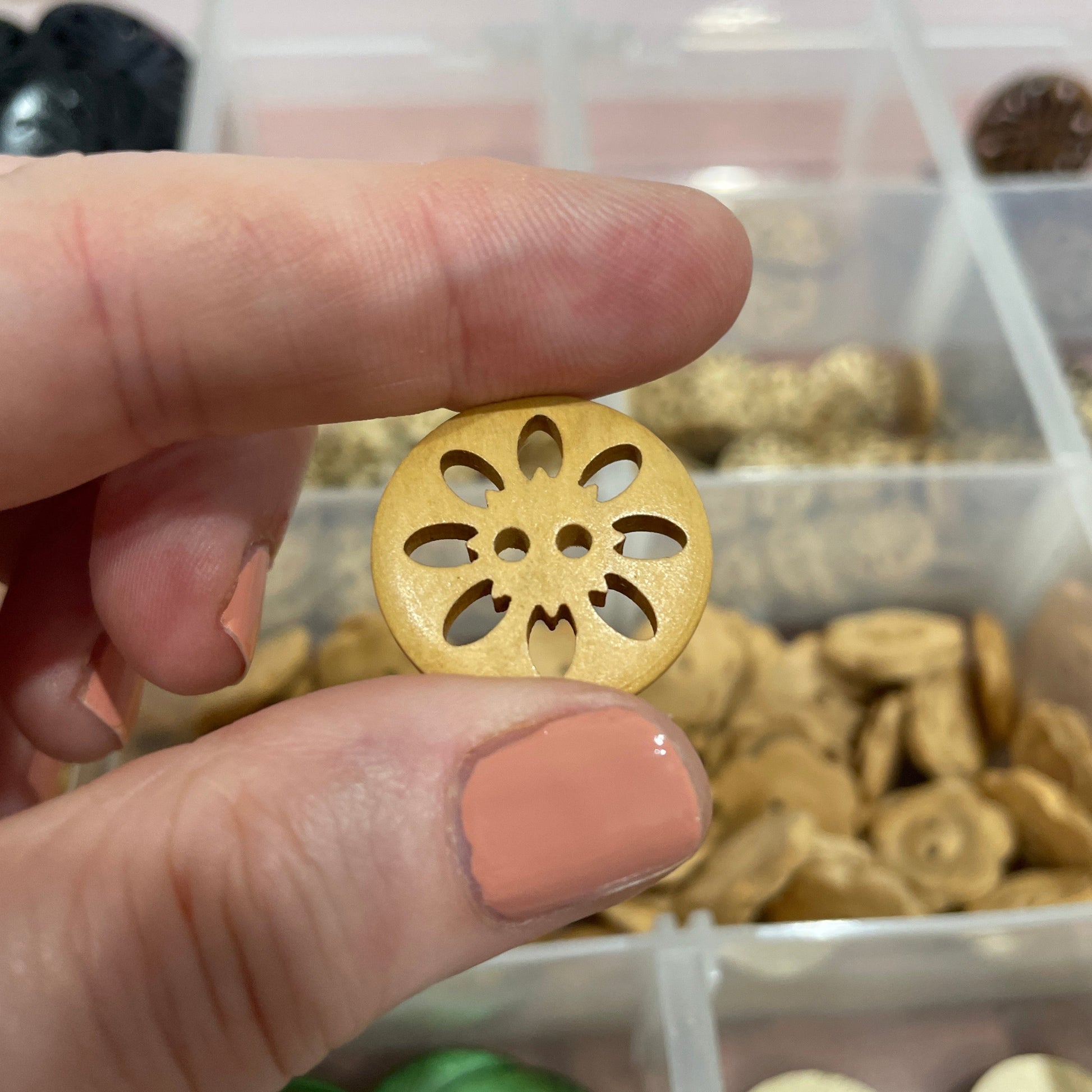 Gold decorative button held between two fingers with a container of buttons in the background