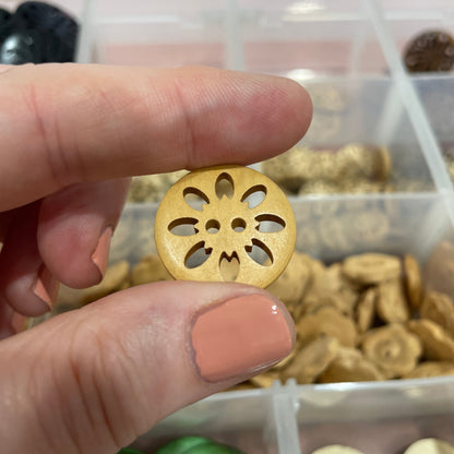 Gold decorative button held between two fingers with a container of buttons in the background