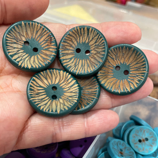 Hand holding decorative buttons with a container of assorted buttons in the background