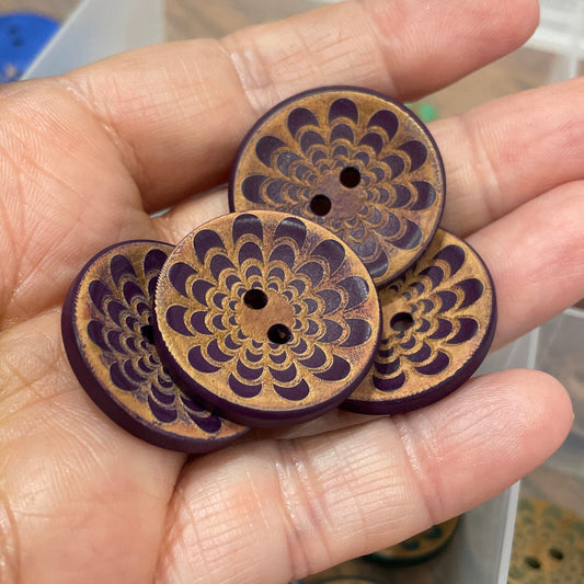 Hand holding decorative wooden buttons with intricate designs, set against a blurred background of more buttons.