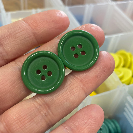 Two green buttons held between fingers with a container of green buttons in the background.