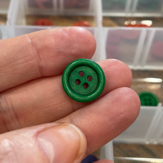 Green button held by a hand with a background of a clear container holding various buttons.