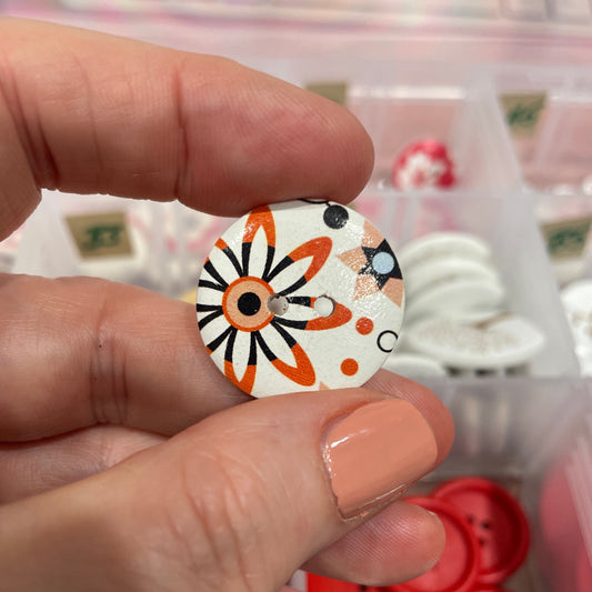 Hand holding a decorative button with a floral design, surrounded by other buttons in the background.