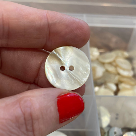 Hand holding a button with a container of buttons in the background