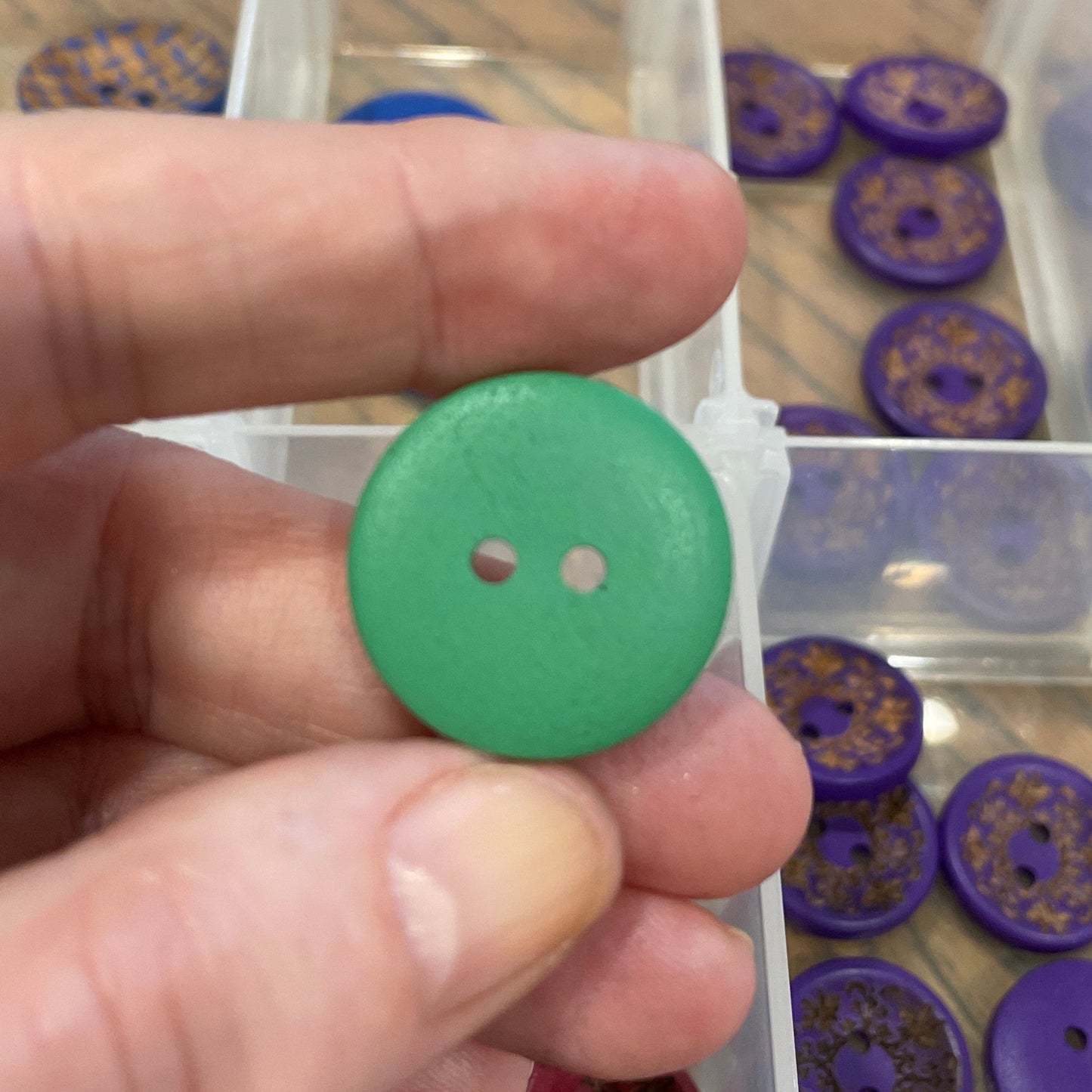 Green button held by a hand with a clear container of buttons in the background