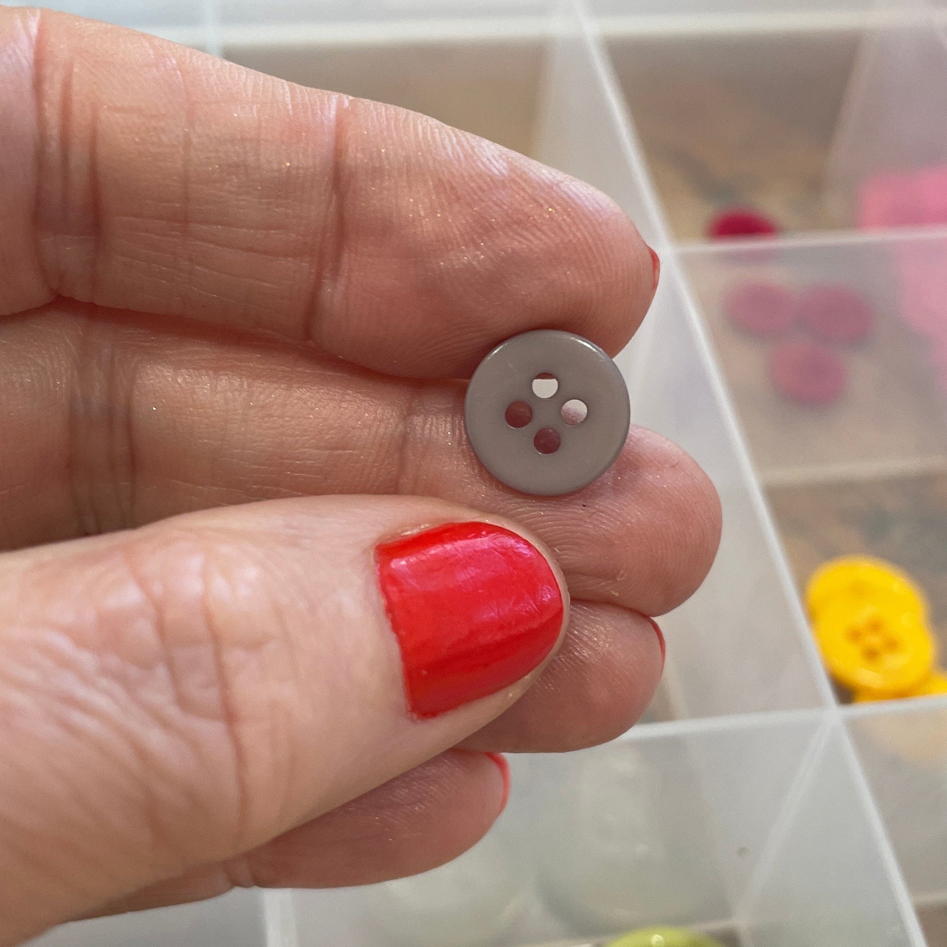 Hand holding a silver button with a clear container of buttons in the background