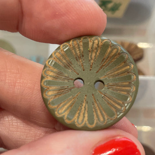 Hand holding a decorative button with a background of various buttons in an organizer.