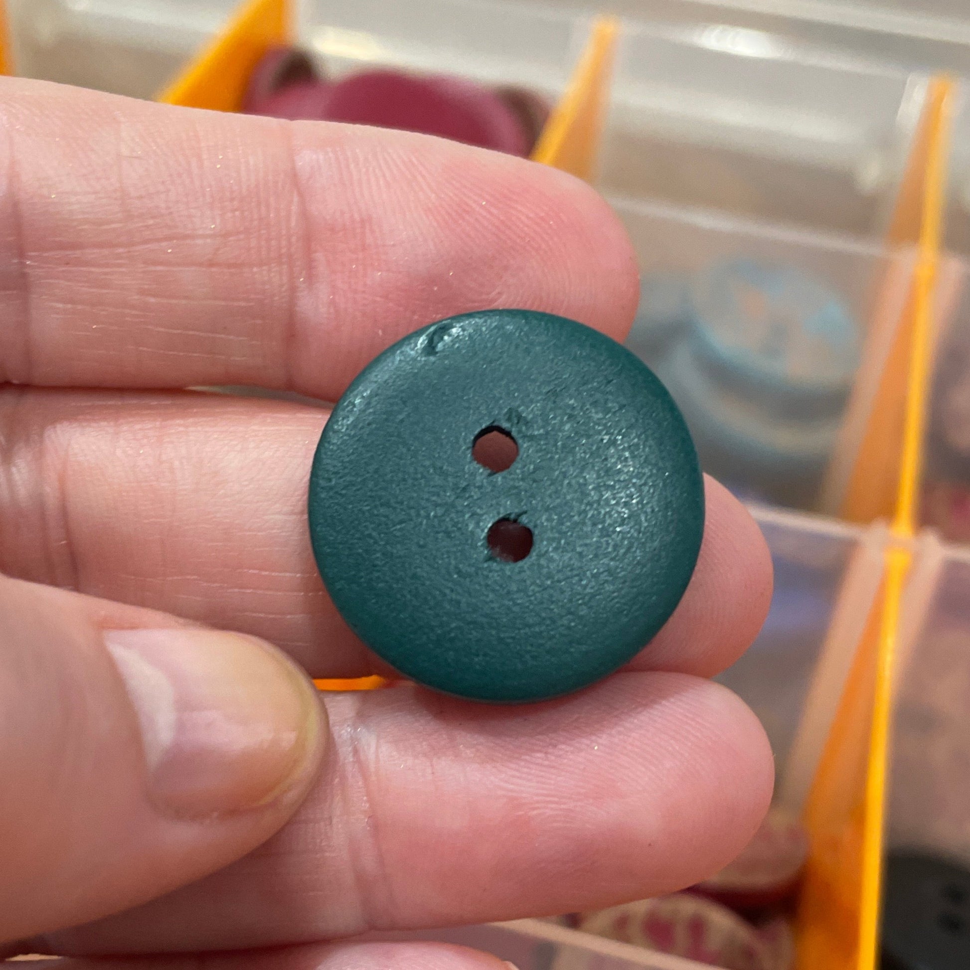 Hand holding a blue button with a clear container of buttons in the background
