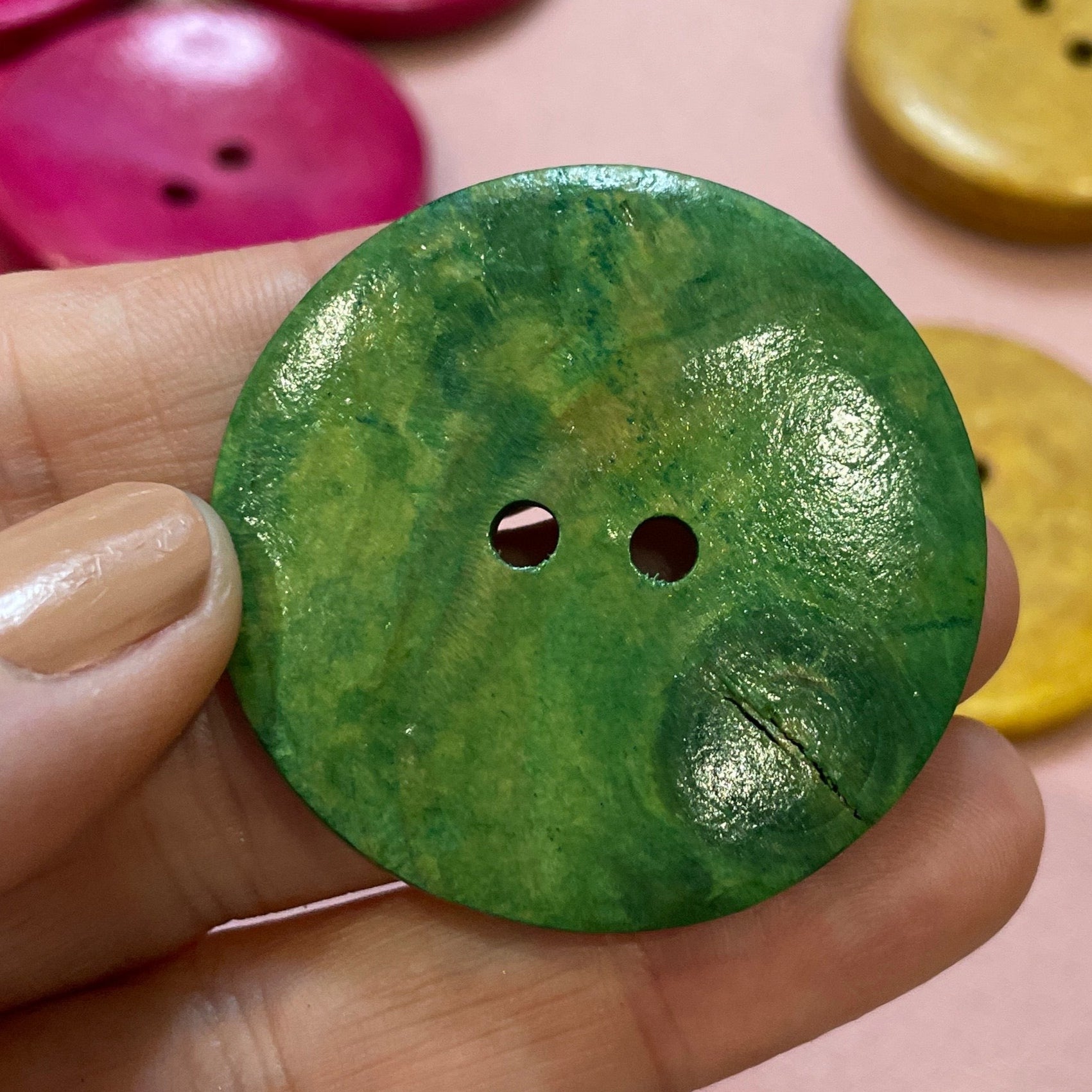 Hand holding a green button with other colorful buttons on a pink surface