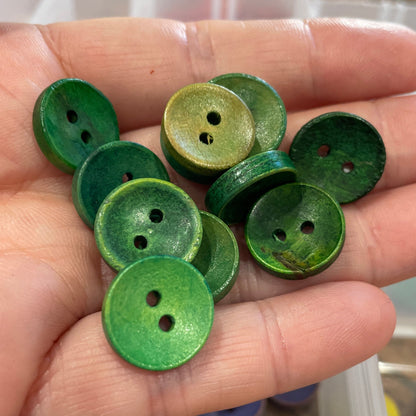 Hand holding green buttons with a container of buttons in the background