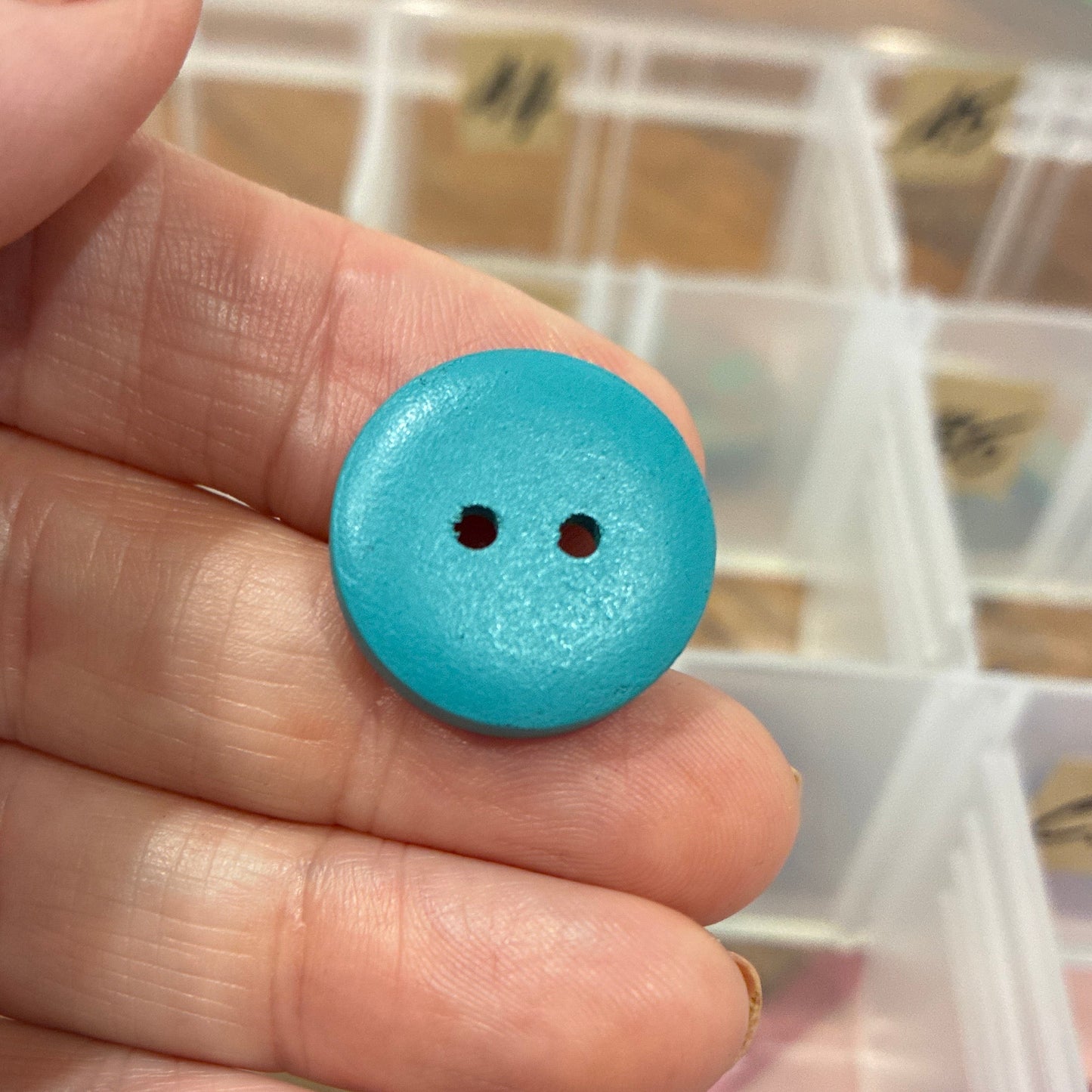 Hand holding a blue button with a clear container of buttons in the background