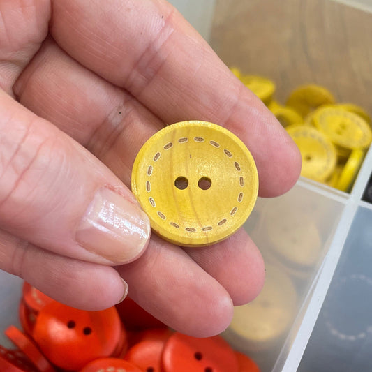 Hand holding a yellow button with a container of orange buttons in the background