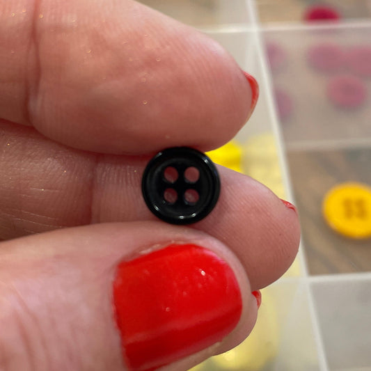Hand holding a small black button with a clear container of colorful buttons in the background