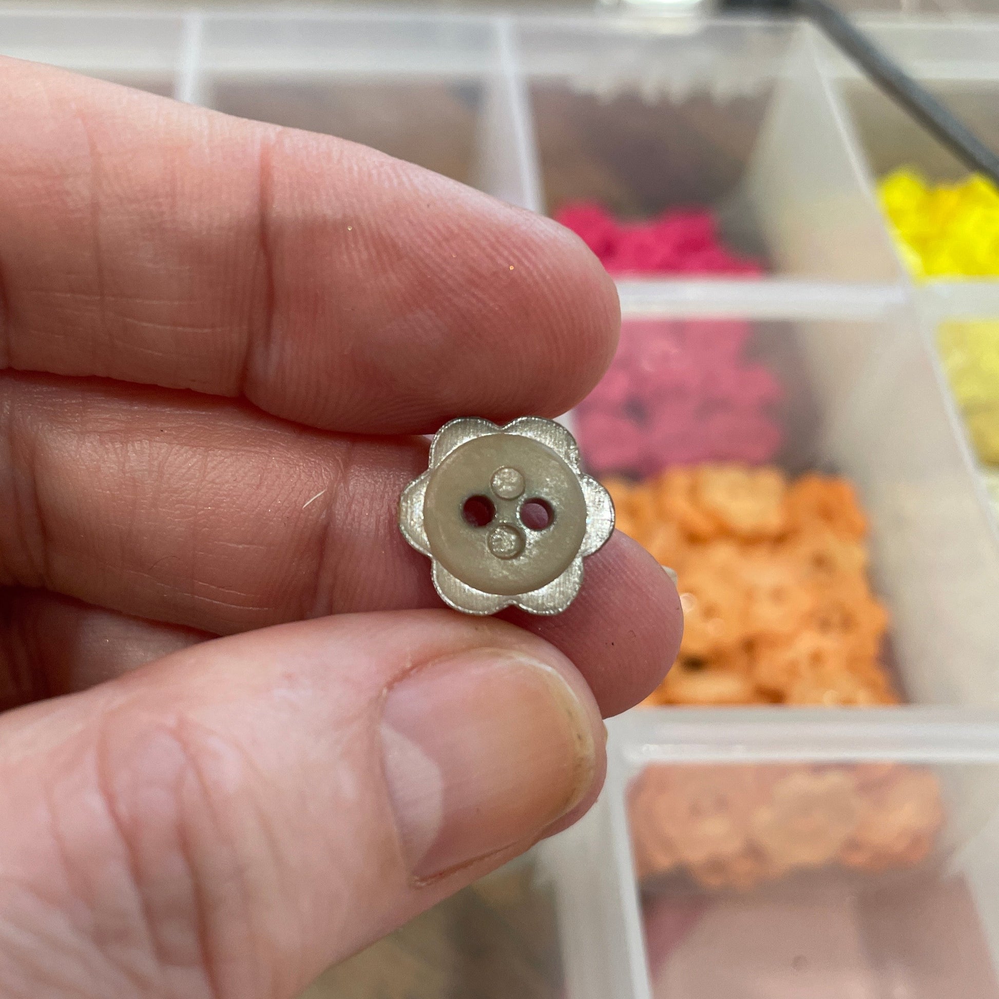 Small metal button held between fingers with a blurred background of colorful items.