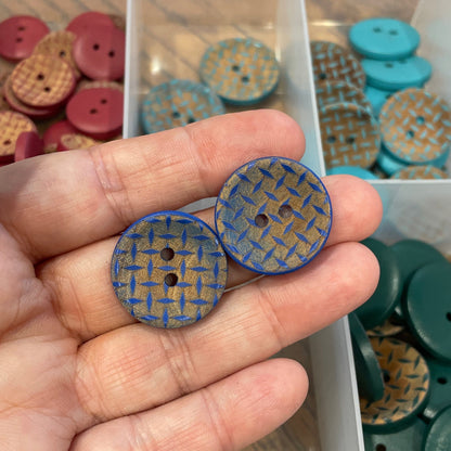 Hand holding two blue buttons with a container of assorted buttons in the background