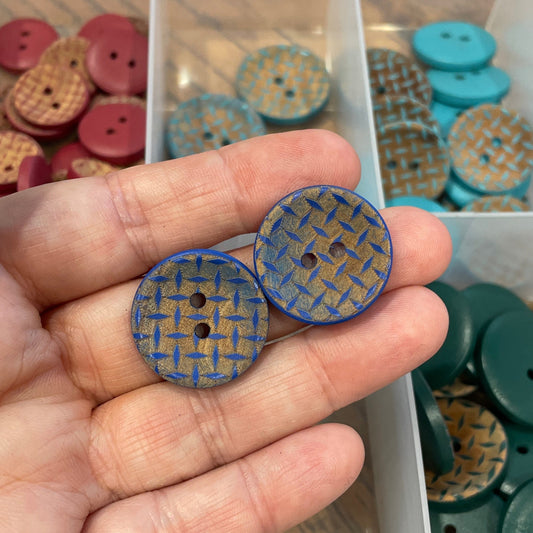 Hand holding two blue buttons with a container of assorted buttons in the background
