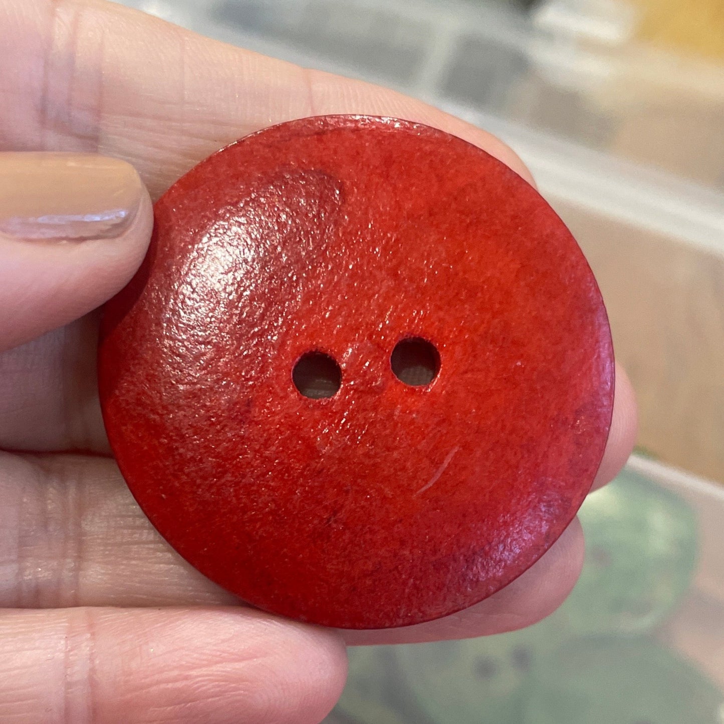 Red button held by a hand with a container of buttons in the background