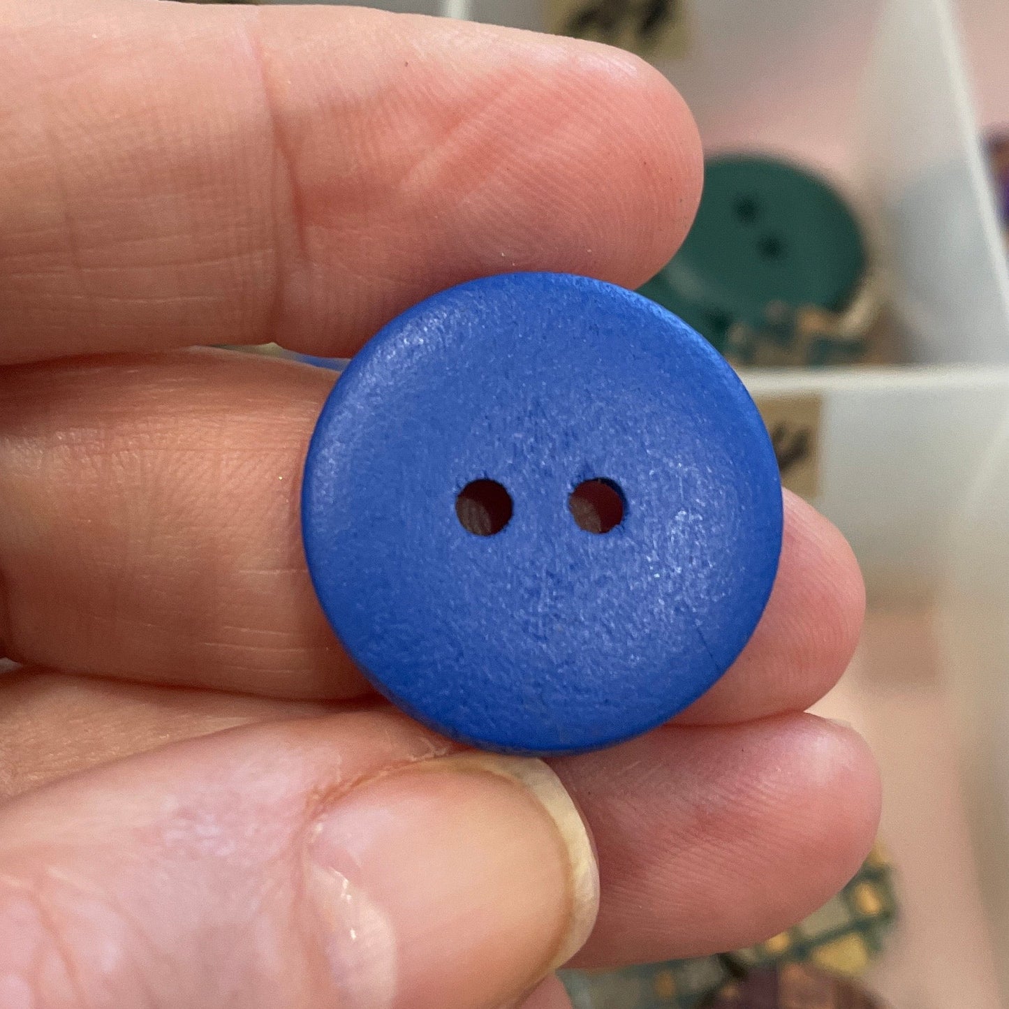 Hand holding a blue button with a blurred background of a button collection.