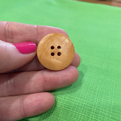 Wooden button held between fingers against a green background