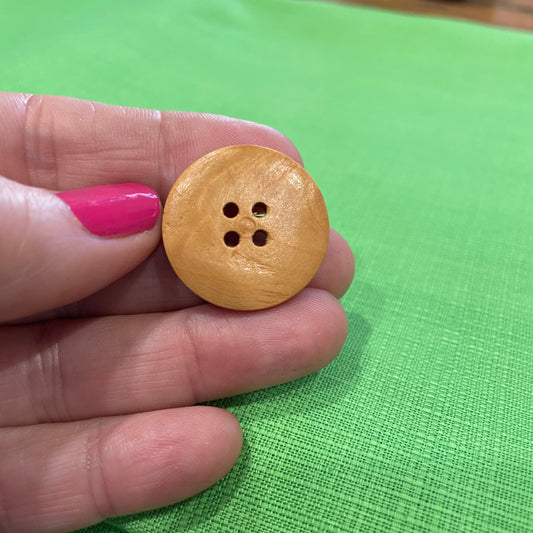 Wooden button held between fingers against a green background