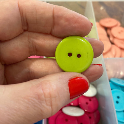 Hand holding a green button with a container of colorful buttons in the background