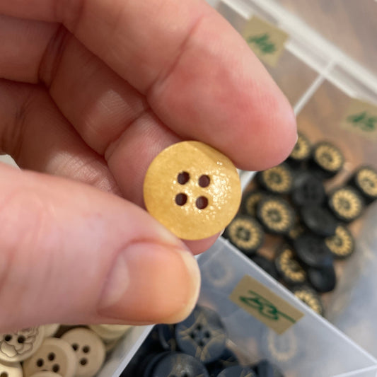 Hand holding a gold button with four holes above a container of buttons.