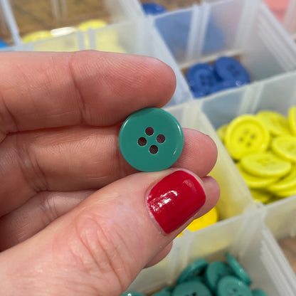 Hand holding a green button with a container of buttons in the background