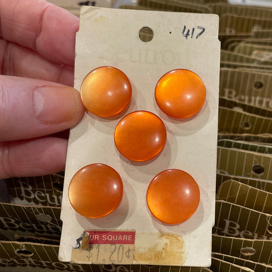 Card with orange buttons held by a hand, with a container of similar cards in the background.