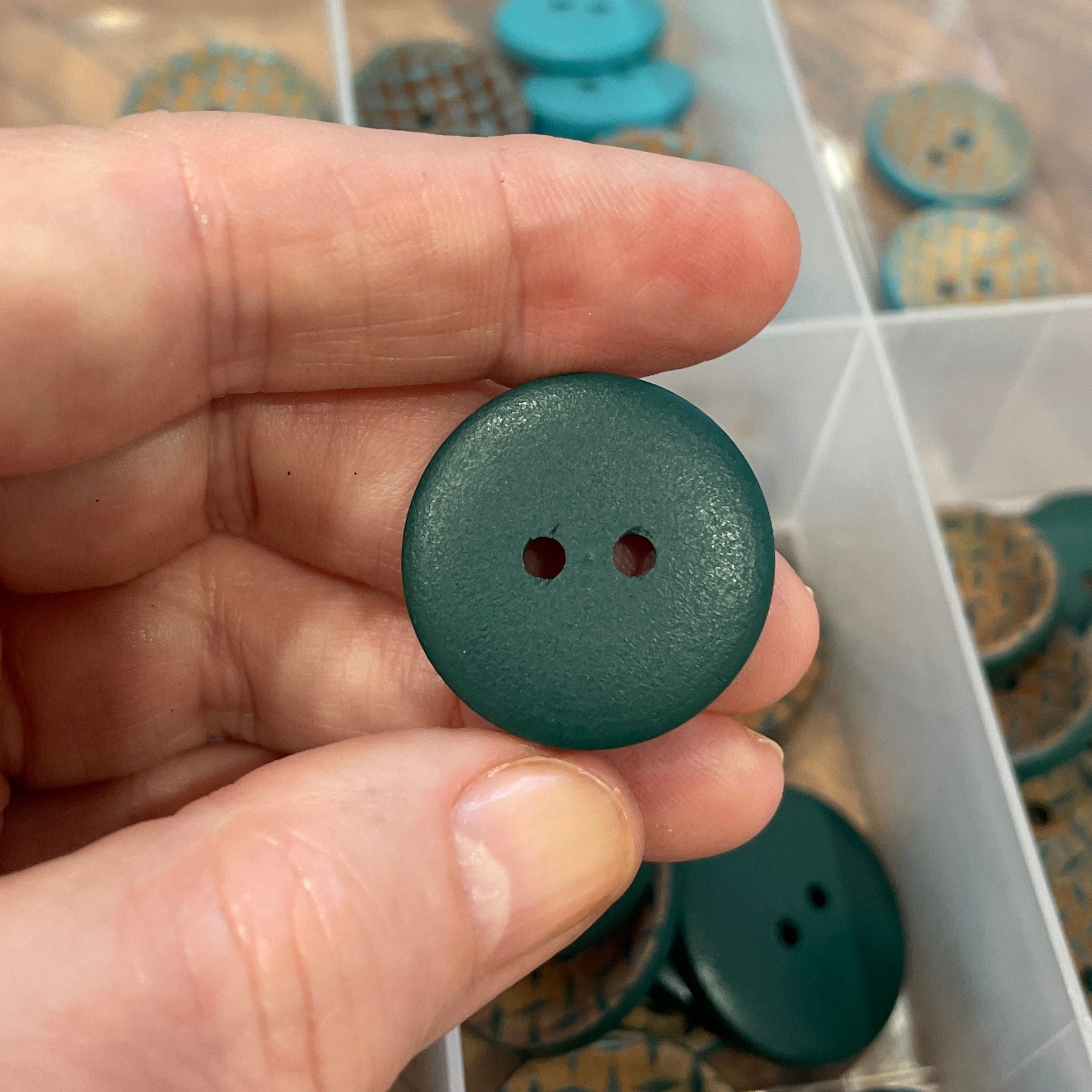 Hand holding a green button with a clear container of buttons in the background