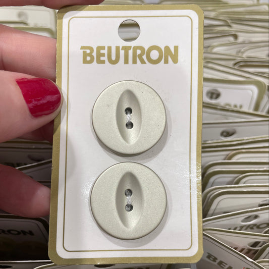 Two buttons on a Beutron branded card held by a hand with red nail polish.