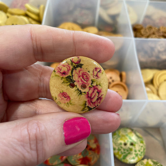 Hand holding a floral button with a background of more buttons in a box