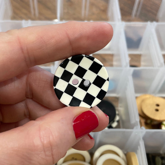 Hand holding a checkered button with a container of buttons in the background