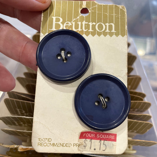 Two blue buttons on a Beltrron card held by a hand with a blurred background.