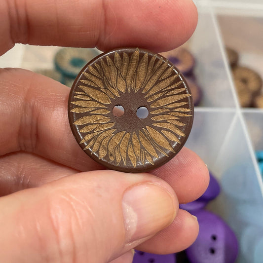 Hand holding a bronze button with a decorative center, against a background of colorful buttons.