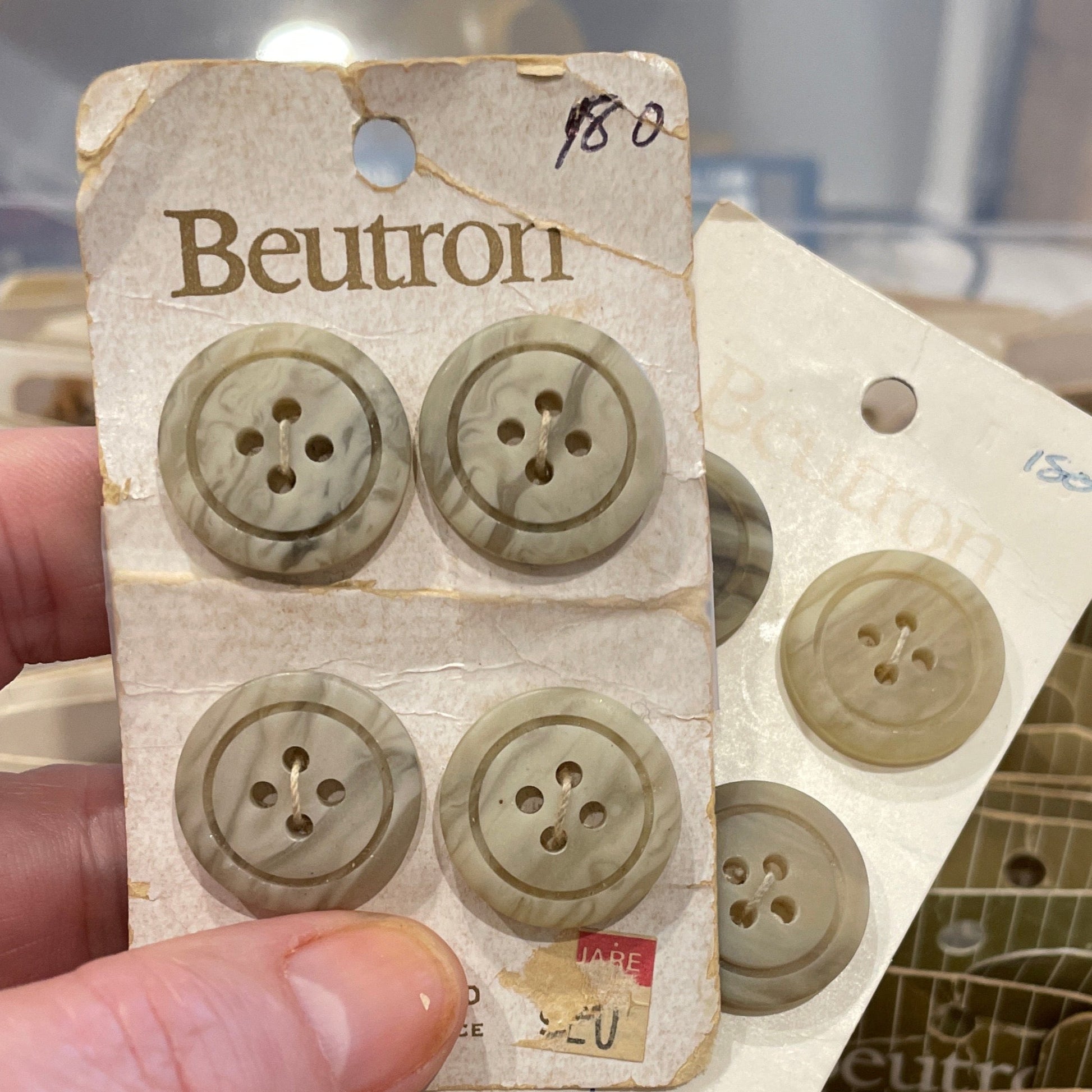 Hand holding a card with four buttons on a blurred background of more buttons and packaging.