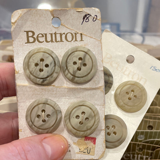 Hand holding a card with four buttons on a blurred background of more buttons and packaging.