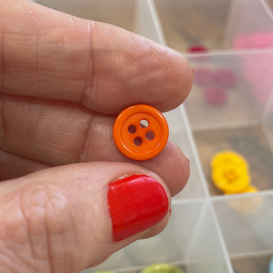 Hand holding two buttons with a clear container of buttons in the background