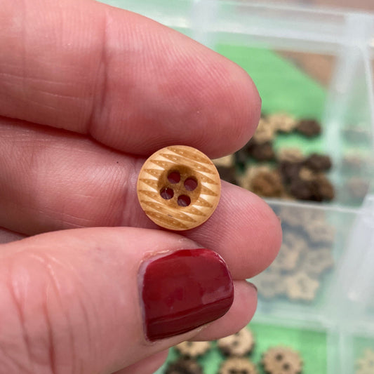 Gold button held between fingers with a container of similar buttons in the background