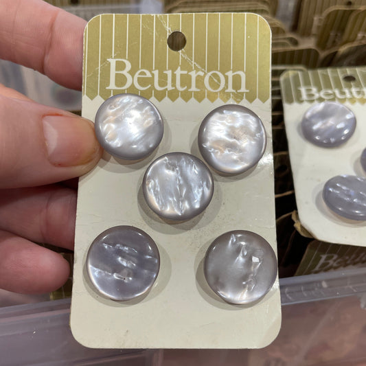 Pack of buttons held by a hand with a brand label in the background