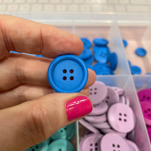 Hand holding a blue button with a container of colorful buttons in the background