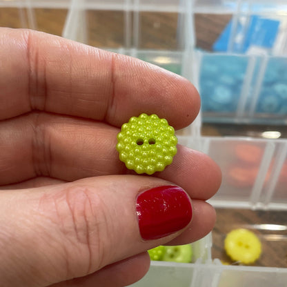 Hand holding a green button with a blurred background of button containers.