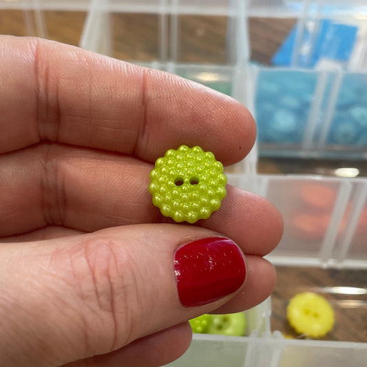 Hand holding a green button with a blurred background of button containers.