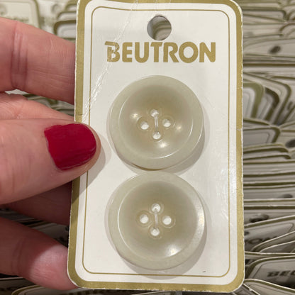 Hand holding a package of Beutron buttons with red nail polish.